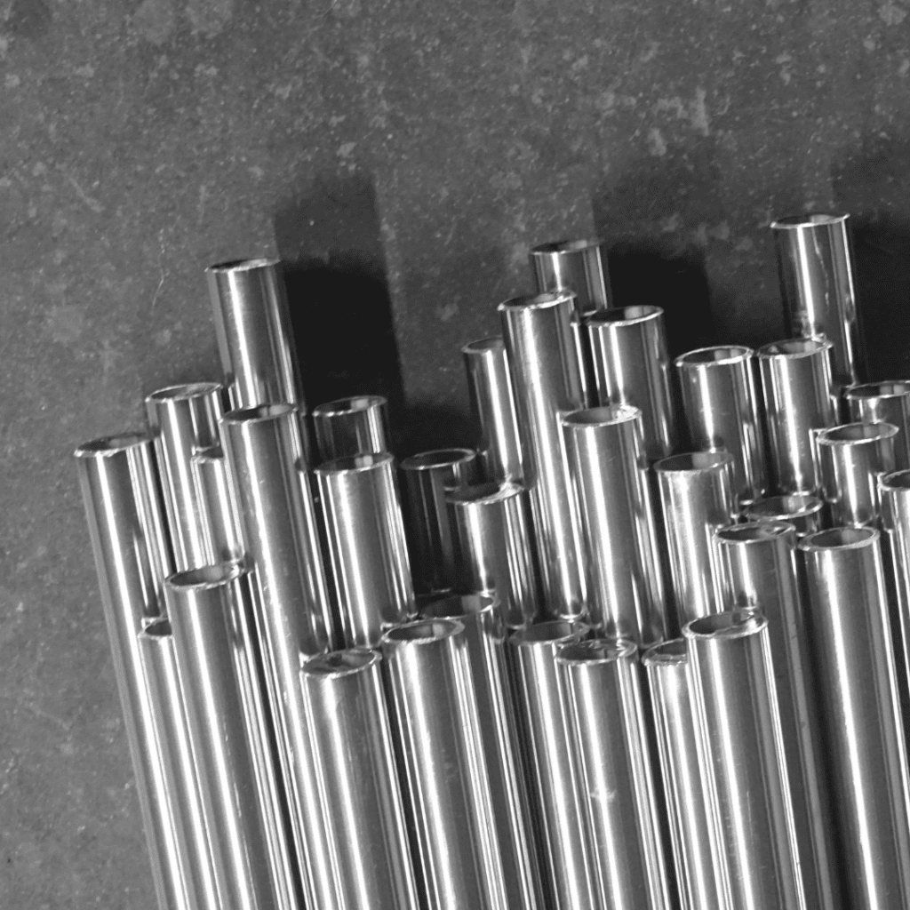 Shiny metal pipes of varying heights are stacked vertically on a dark, textured surface.