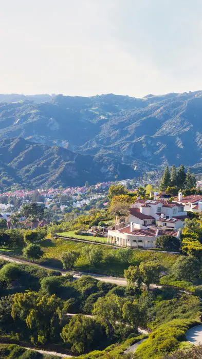 Mansions on a green hillside with mountains rising in the background.