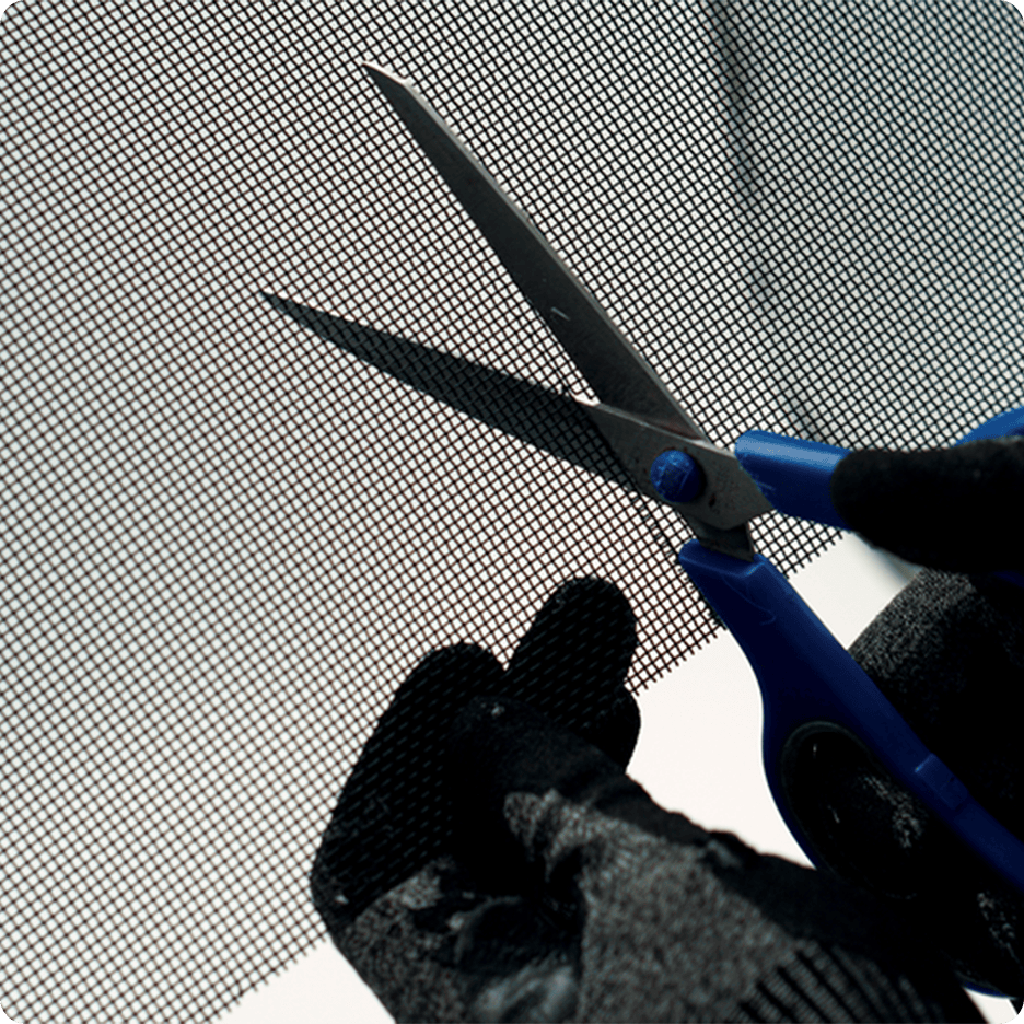 Gloved hands use blue scissors to cut mesh screen.