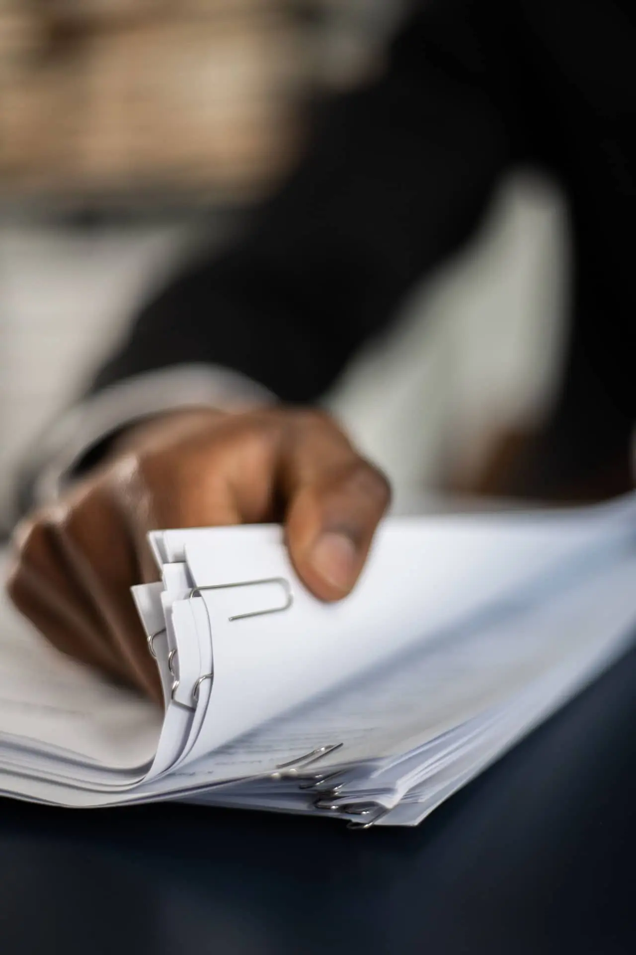 A hand flips through clipped papers on a desk.