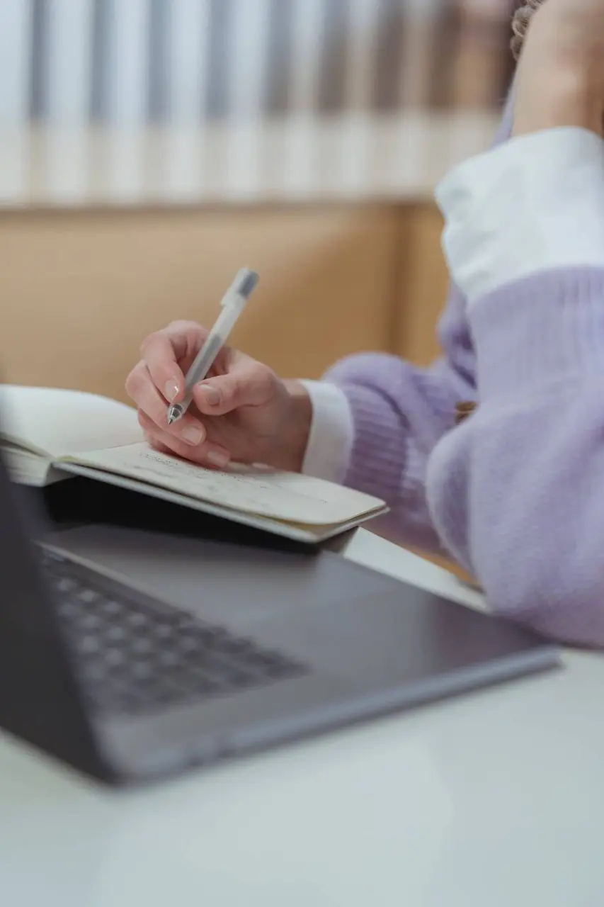 Handwriting in a notebook beside a laptop on a desk.