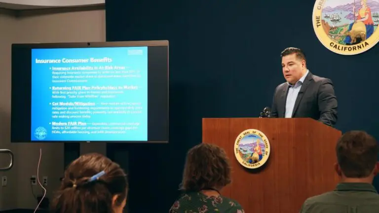 A man speaks at a podium next to a screen displaying insurance consumer benefits in California.