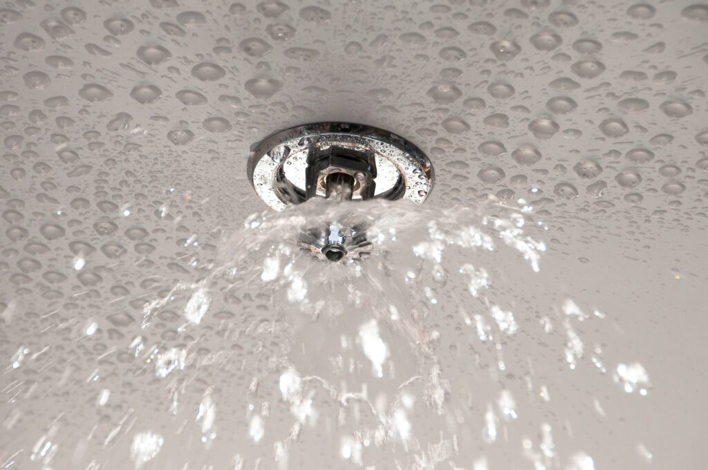 Fire sprinkler on ceiling releasing water.